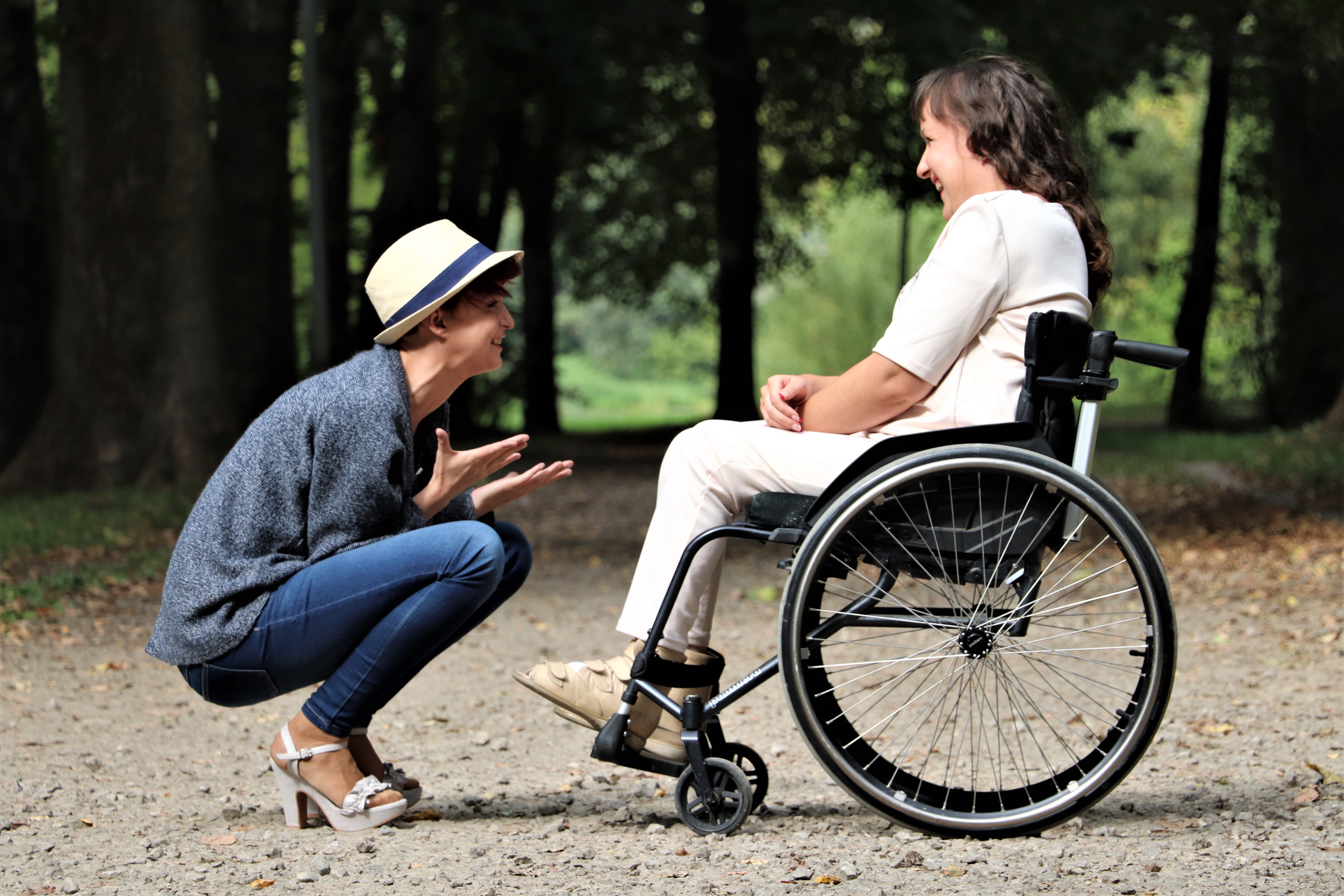 Zwei Frauen unterhalten sich angeregt. Eine sitzt im Rollstuhl, eine ist in der Hocke.
